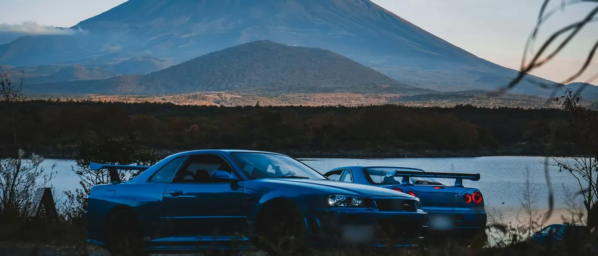 Two blue Skyline GT-Rs by a lake